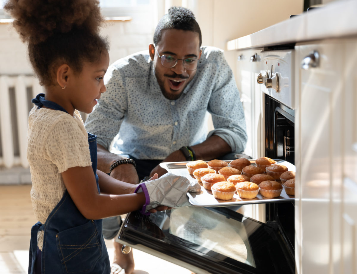 Excited dad watching daughter taking muffins out of oven